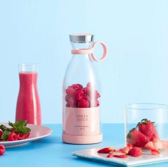 Glass bottle with pink base and silver top, filled with raspberries, on a blue background with a glass of pink juice and strawberries